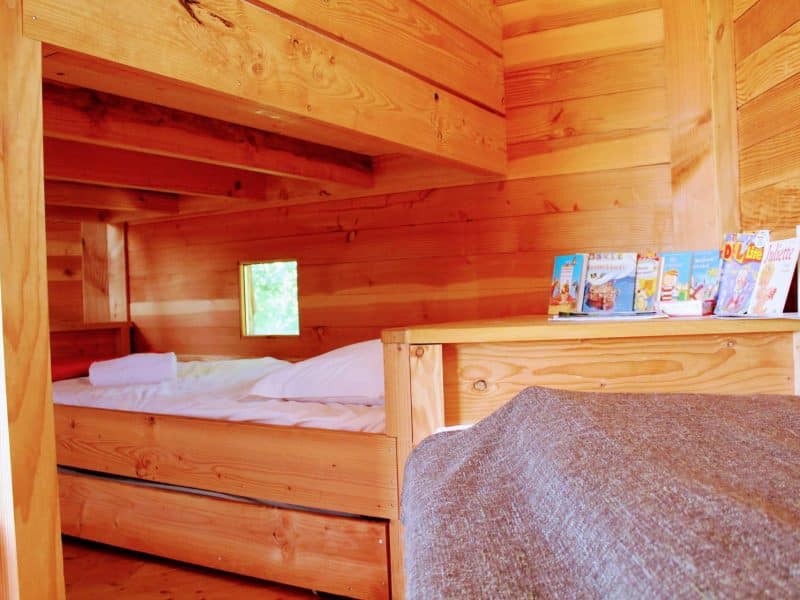 Cabane en bois chaleureuse avec lit douillet et fenêtres lumineuses.