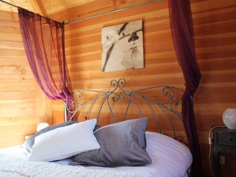 Chalet en bois avec lit en fer forgé et drapés violets élégants.
