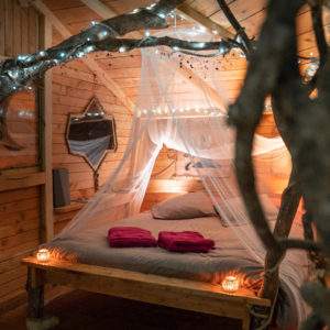 Cabane en bois romantique avec lit à baldaquin et lumières douces.