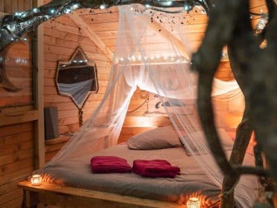 Cabane en bois romantique avec lit à baldaquin et lumières douces.