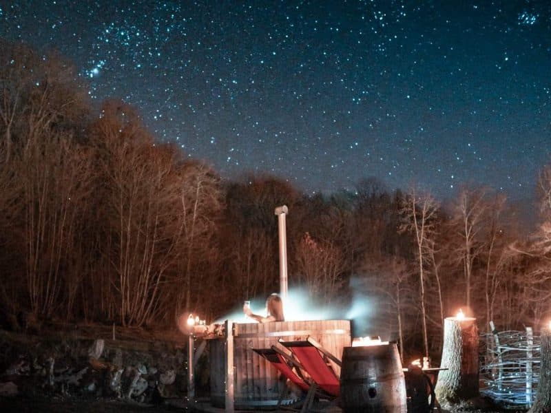 Cabane en bois sous un ciel étoilé, avec des chaises confortables et un feu chaleureux.