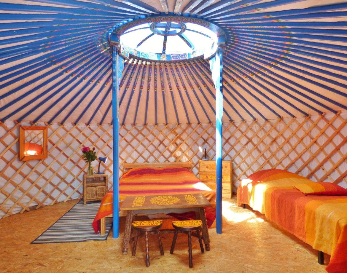 Yourte colorée en Auvergne, avec un lit central et des décorations chaleureuses.