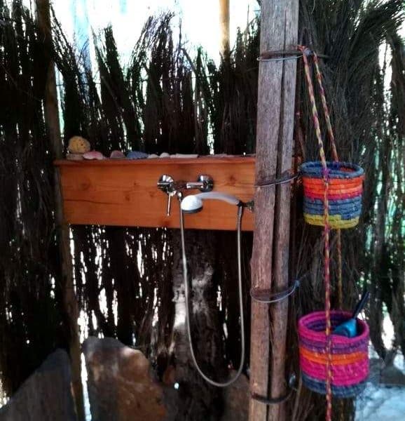 Douche extérieure en bois, entourée de plantes, dans un hébergement écologique.