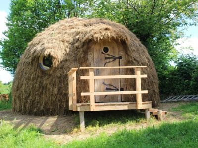 Hébergement insolite en forme de dôme en paille, avec une porte en bois accueillante.