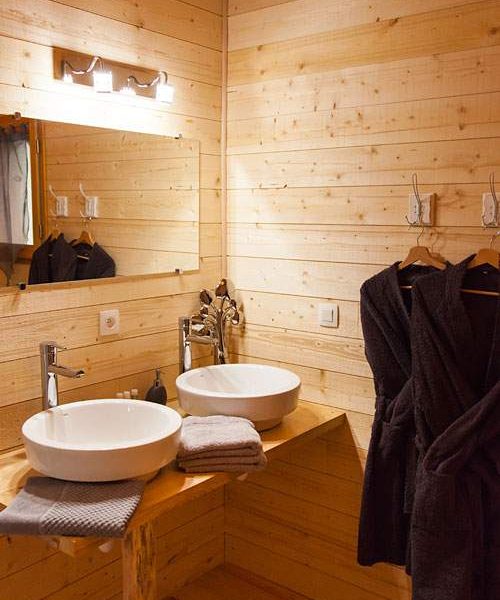 Salle de bain en bois avec deux lavabos et peignoirs suspendus.