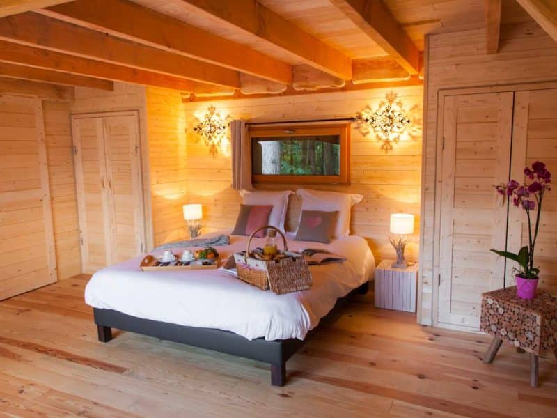 Chalet en bois avec lit douillet et petit-déjeuner sur un plateau. Ambiance chaleureuse.