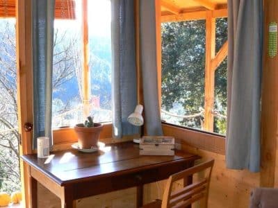 Cabane en bois lumineuse avec vue sur la nature, bureau en bois et rideaux bleus.