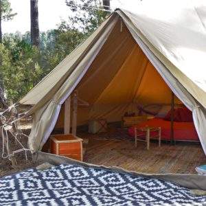 Tente safari spacieuse en pleine nature, avec un lit douillet et un tapis coloré.