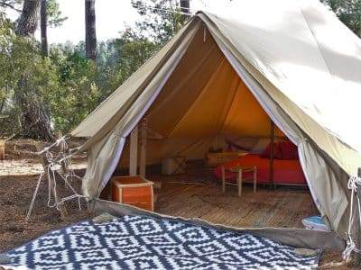 Tente safari spacieuse en pleine nature, avec un lit douillet et un tapis coloré.