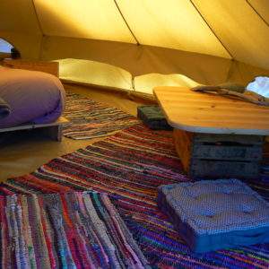 Tente glamping cosy avec un lit douillet et des tapis colorés au sol.