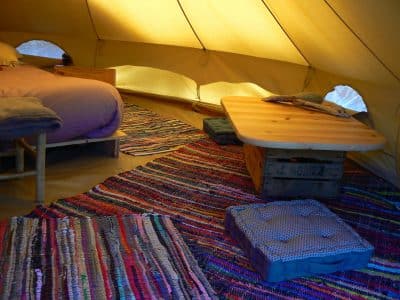 Tente glamping cosy avec un lit douillet et des tapis colorés au sol.