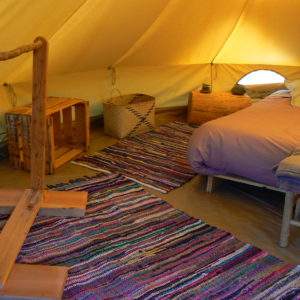 Tente glamping cosy avec lit douillet et tapis coloré, au cœur du Languedoc-Roussillon.