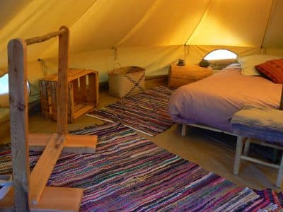 Tente glamping cosy avec lit douillet et tapis coloré, au cœur du Languedoc-Roussillon.