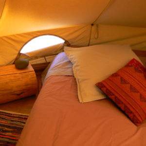 Tente glamping cosy avec lit douillet et coussins colorés, au cœur du Languedoc-Roussillon.