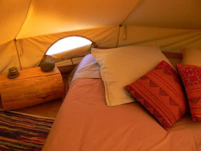 Tente glamping cosy avec lit douillet et coussins colorés, au cœur du Languedoc-Roussillon.