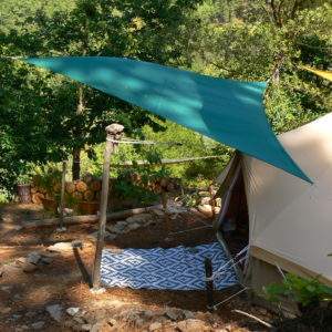 Tente safari au cœur de la nature, abritée sous un auvent vert et entourée de verdure.