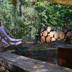Hébergement insolite en pleine nature, avec chaises longues et bois empilé en arrière-plan.