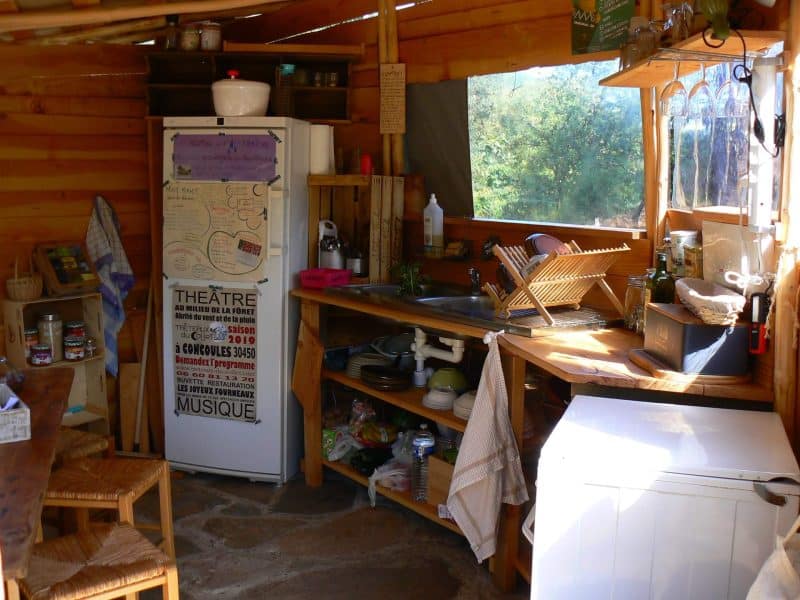 Cabane en bois avec cuisine rustique, frigo et vue sur la nature.