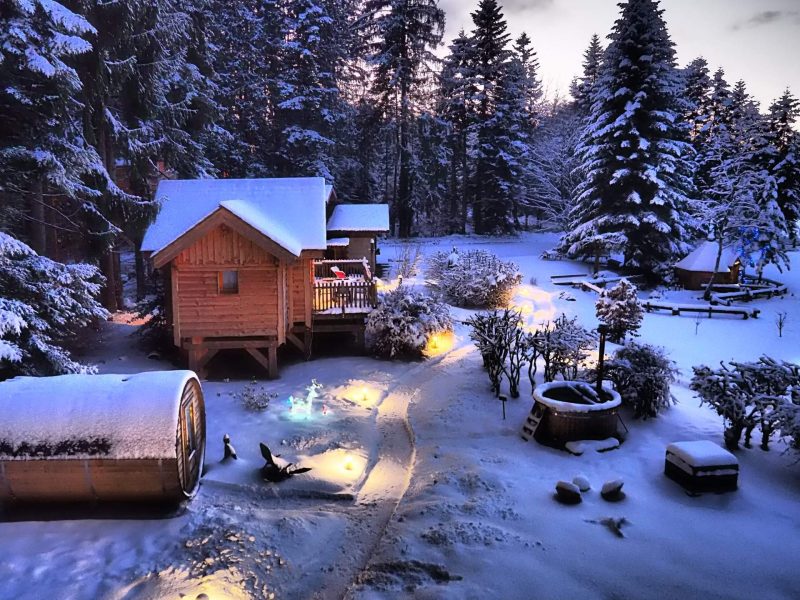 Chalet en bois dans un paysage enneigé, illuminé par des lumières douces.