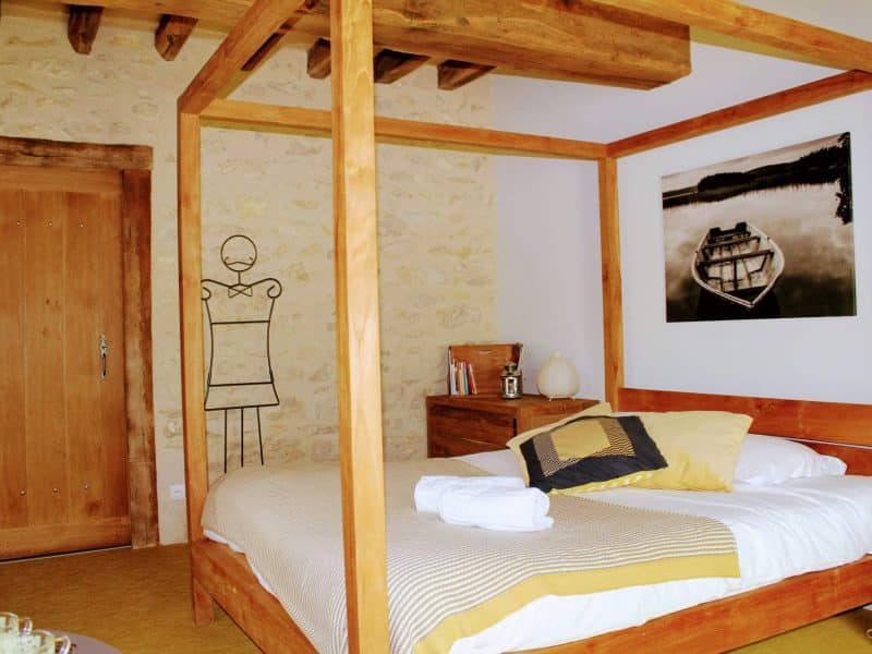 Chambre dhôtes avec lit à baldaquin et mur en pierre apparente.