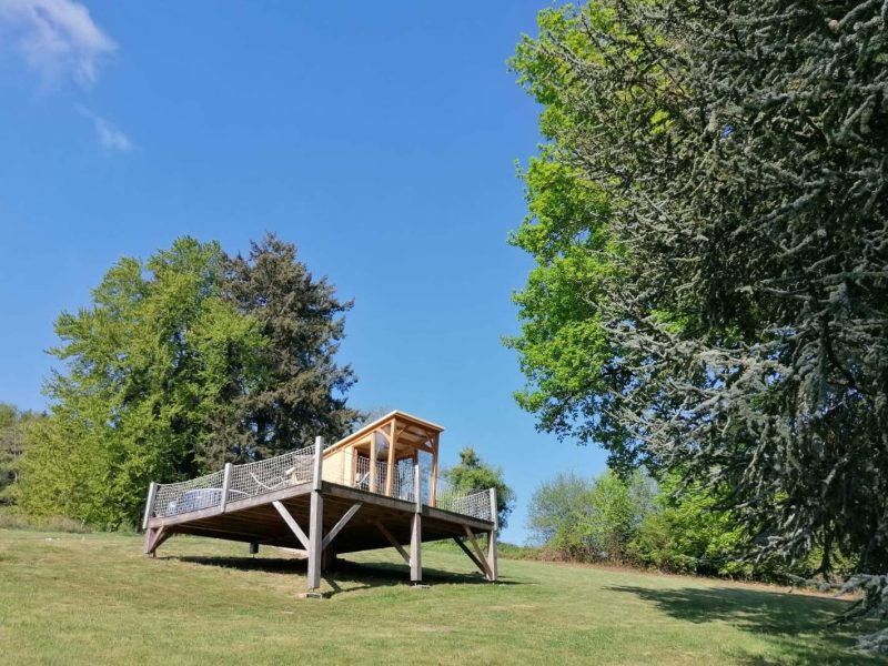 Cabane sur pilotis entourée darbres, avec un ciel bleu dégagé.