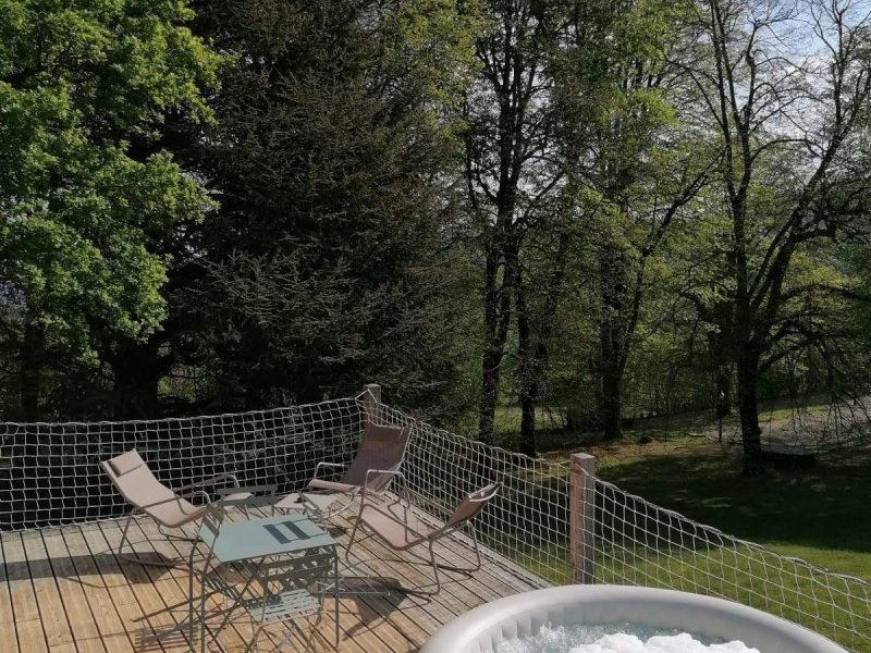 Chalet avec terrasse, jacuzzi et vue sur la nature verdoyante environnante.