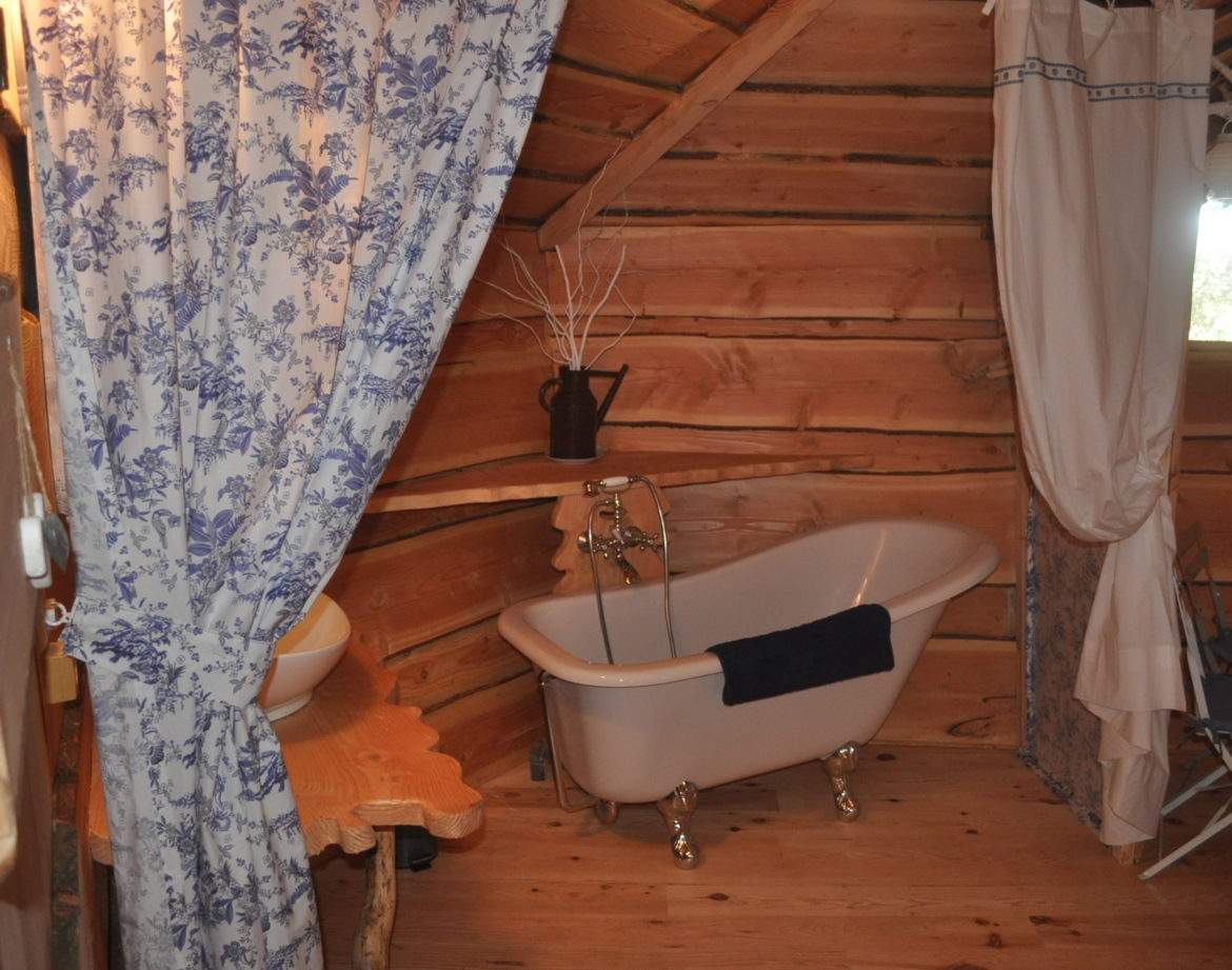 Cabane en bois avec baignoire vintage et décor floral, idéale pour un séjour romantique.