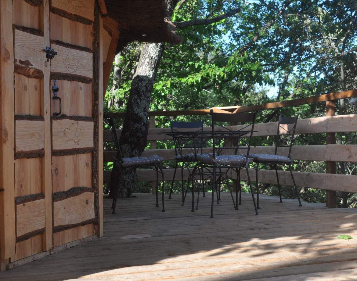 Cabane perchée en bois avec terrasse et chaises, entourée de verdure en Auvergne.