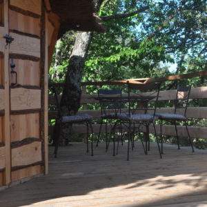 Cabane perchée en bois avec terrasse et chaises, entourée de verdure en Auvergne.