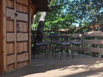 Cabane perchée en bois avec terrasse et chaises, entourée de verdure en Auvergne.