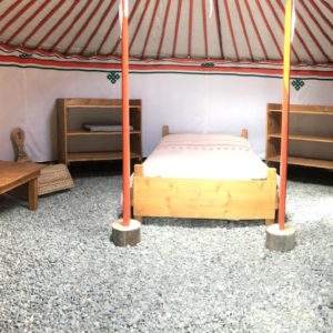 Yourte spacieuse en Auvergne-Rhône-Alpes, avec lit en bois et mobilier en osier.