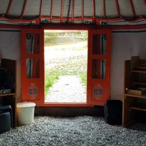 Yourte accueillante avec portes orange, offrant une vue sur la nature environnante.