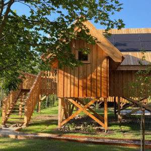 Cabane en bois sur pilotis, avec panneaux solaires, entourée de verdure en Provence.