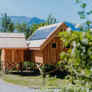 Cabane en bois perchée avec panneaux solaires, vue sur les montagnes environnantes.