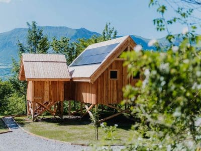 Cabane en bois perchée avec panneaux solaires, vue sur les montagnes environnantes.
