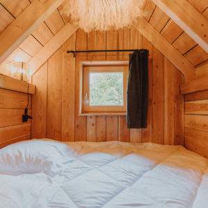 Cabane en bois chaleureuse avec un lit douillet et une fenêtre lumineuse.