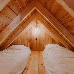 Chalet en bois avec lit douillet sous un toit en pente, ambiance chaleureuse.