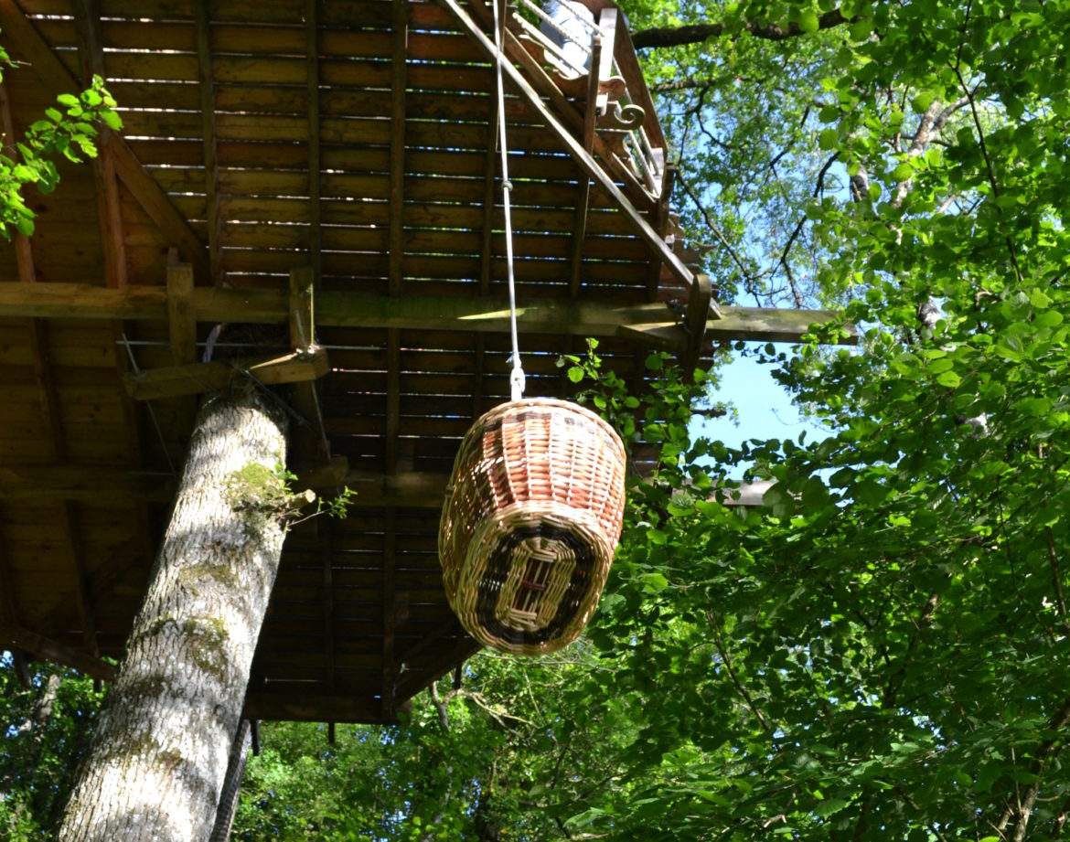 Cabane perchée dans les arbres, avec un panier suspendu au-dessus de la verdure.