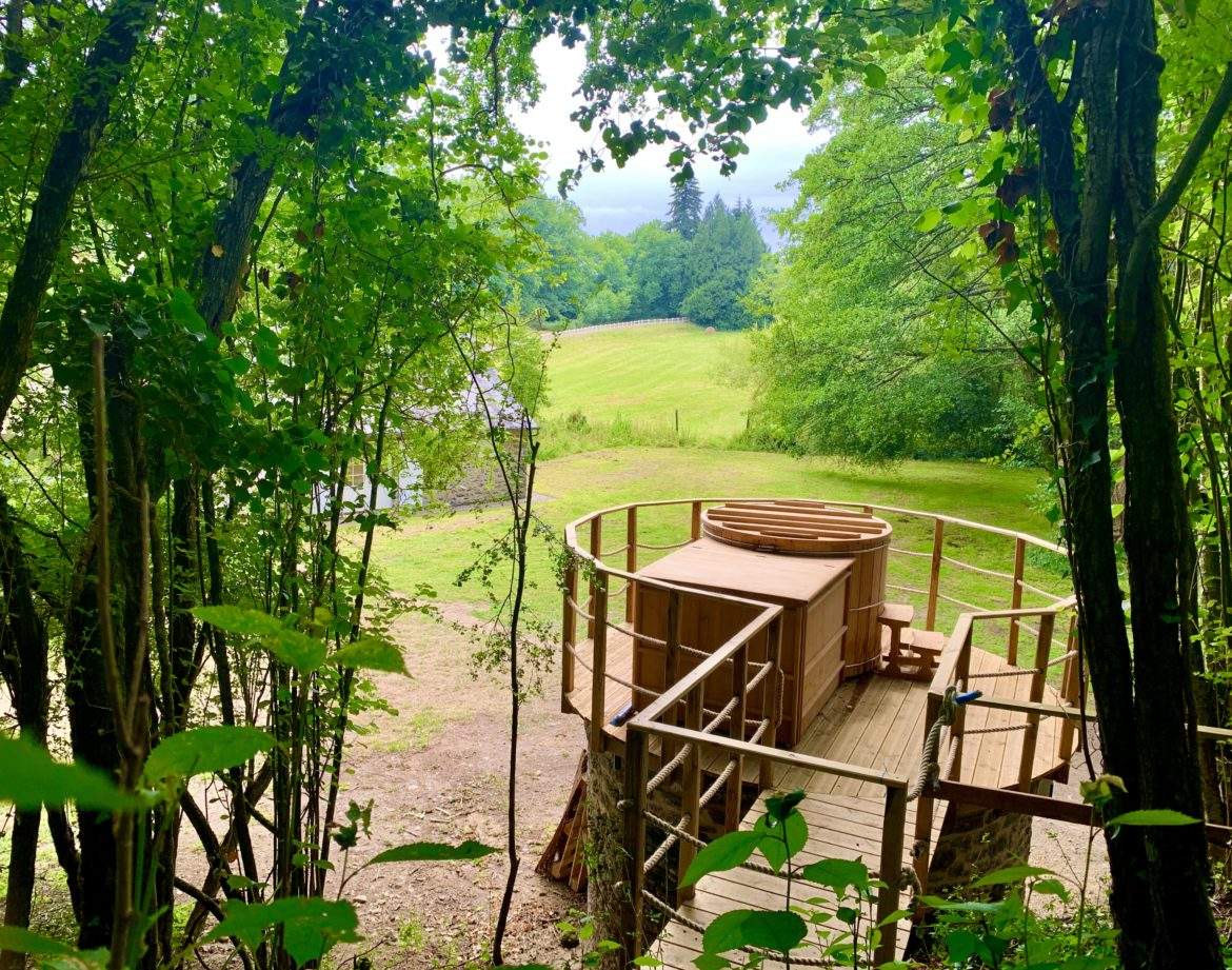 Cabane perchée en bois, entourée de verdure, offrant une vue sur la nature.