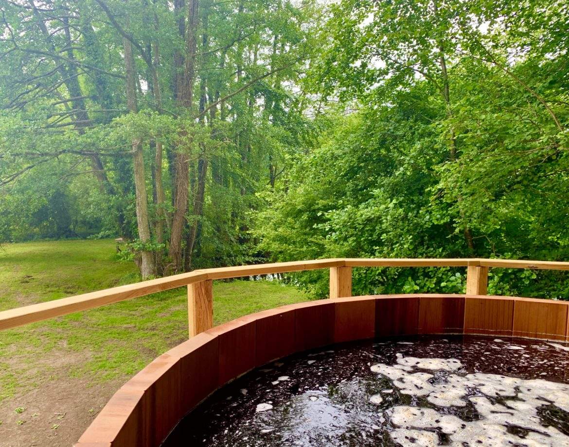 Hébergement insolite en Pays de la Loire avec un jacuzzi en bois entouré de verdure.
