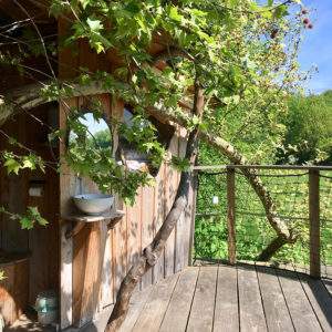 Cabane perchée en bois, intégrée à la nature, avec un lavabo en extérieur.