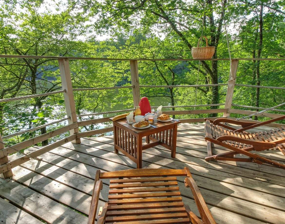 Cabane perchée dans les arbres, terrasse en bois avec vue sur la nature verdoyante.
