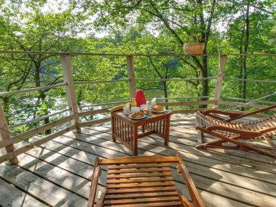 Cabane perchée dans les arbres, terrasse en bois avec vue sur la nature verdoyante.