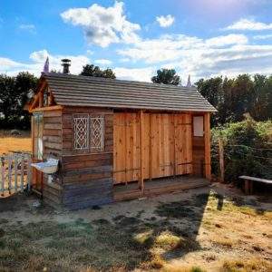 Cabane en bois charmante, avec un toit en pente et un jardin verdoyant.