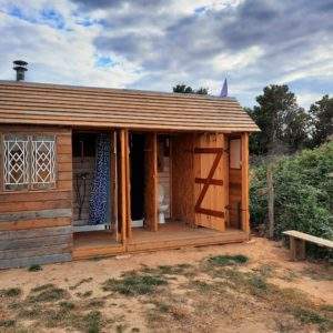 Cabane en bois atypique avec toit en pente, située dans un cadre naturel.