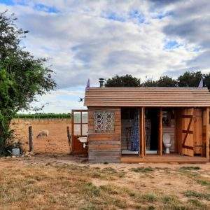Cabane en bois avec toilettes extérieures, entourée de champs et danimaux.