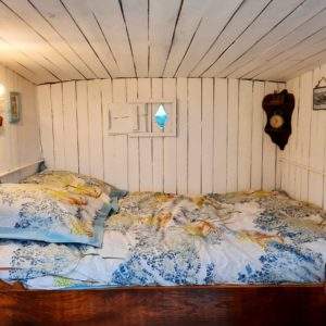 Cabane insolite avec lit douillet et murs en bois blanc, ambiance chaleureuse.