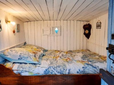 Cabane insolite avec lit douillet et murs en bois blanc, ambiance chaleureuse.