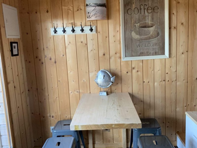 Cabane en bois avec table en bois et chaises métalliques, ambiance chaleureuse.