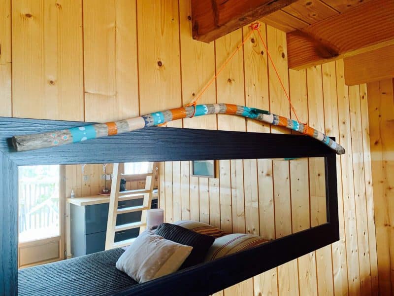 Cabane en bois avec un miroir décoré dune branche colorée et murs en bois naturel.